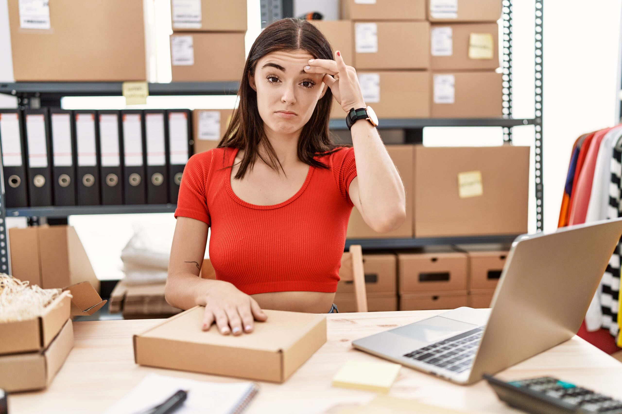 Young hispanic woman preparing order working at storehouse worried and stressed about a problem with hand on forehead, nervous and anxious for crisis